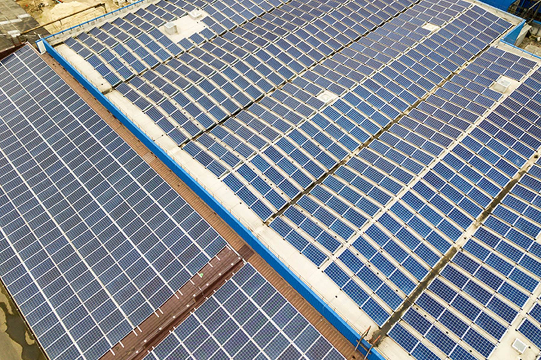 Aerial view of solar power plant with blue photovoltaic panels mounted of industrial building roof.