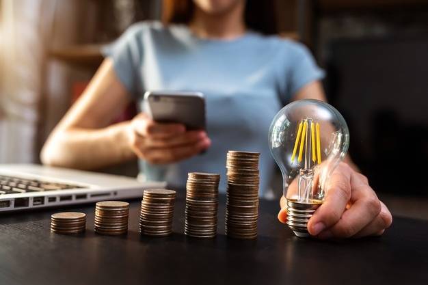 mao-de-negocios-segurando-a-lampada-com-o-uso-de-computador-portatil-e-a-pilha-de-dinheiro-no-escritorio-ideia-de-economia-de-energia-e-conceito-de-contabilidade-financeira_71455-41